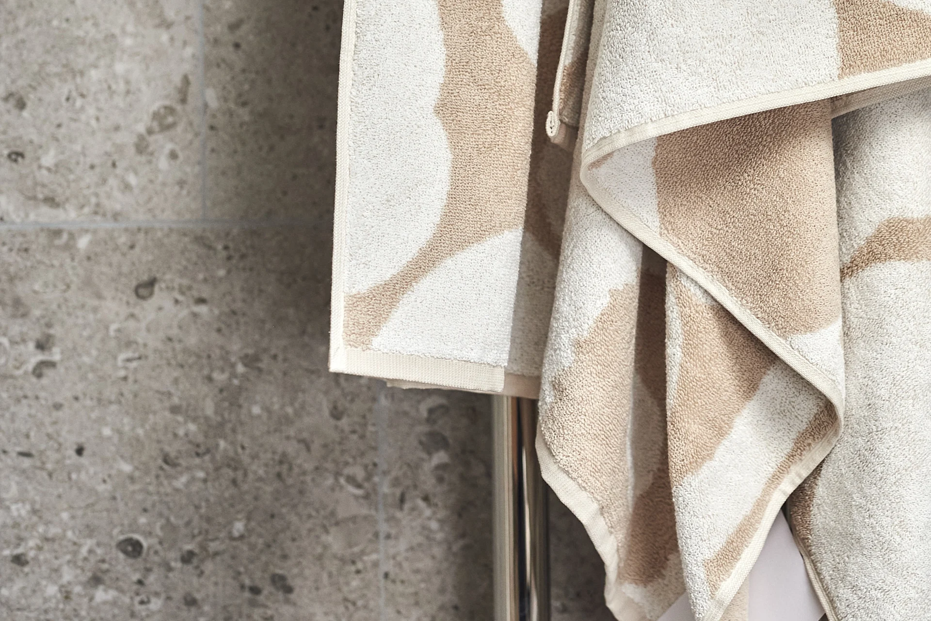 Beige and cream patterned towels hang on a metal rail against a grey wall.