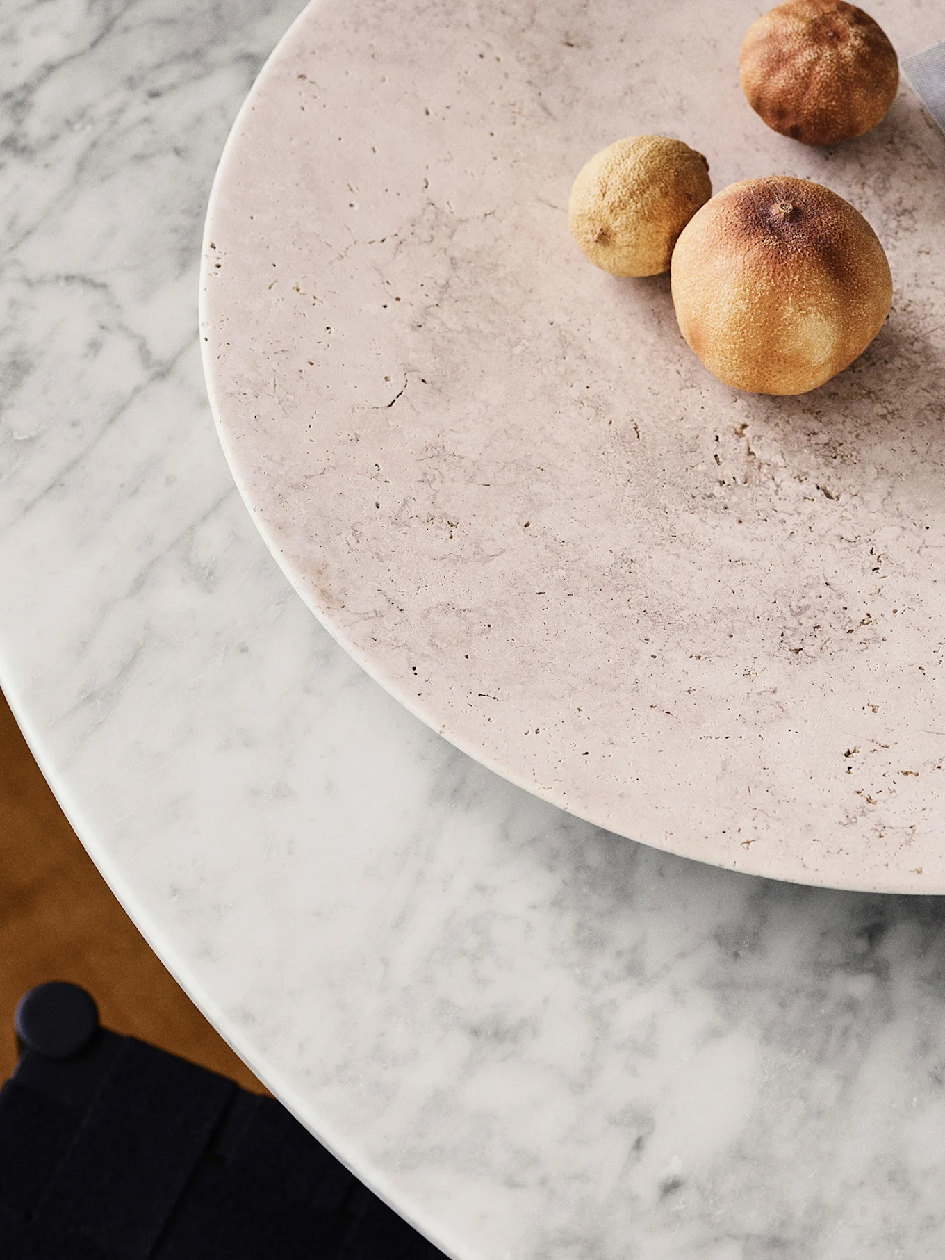 Three dried citrus fruits on a light pink travertine plate, resting on a white marble table.
