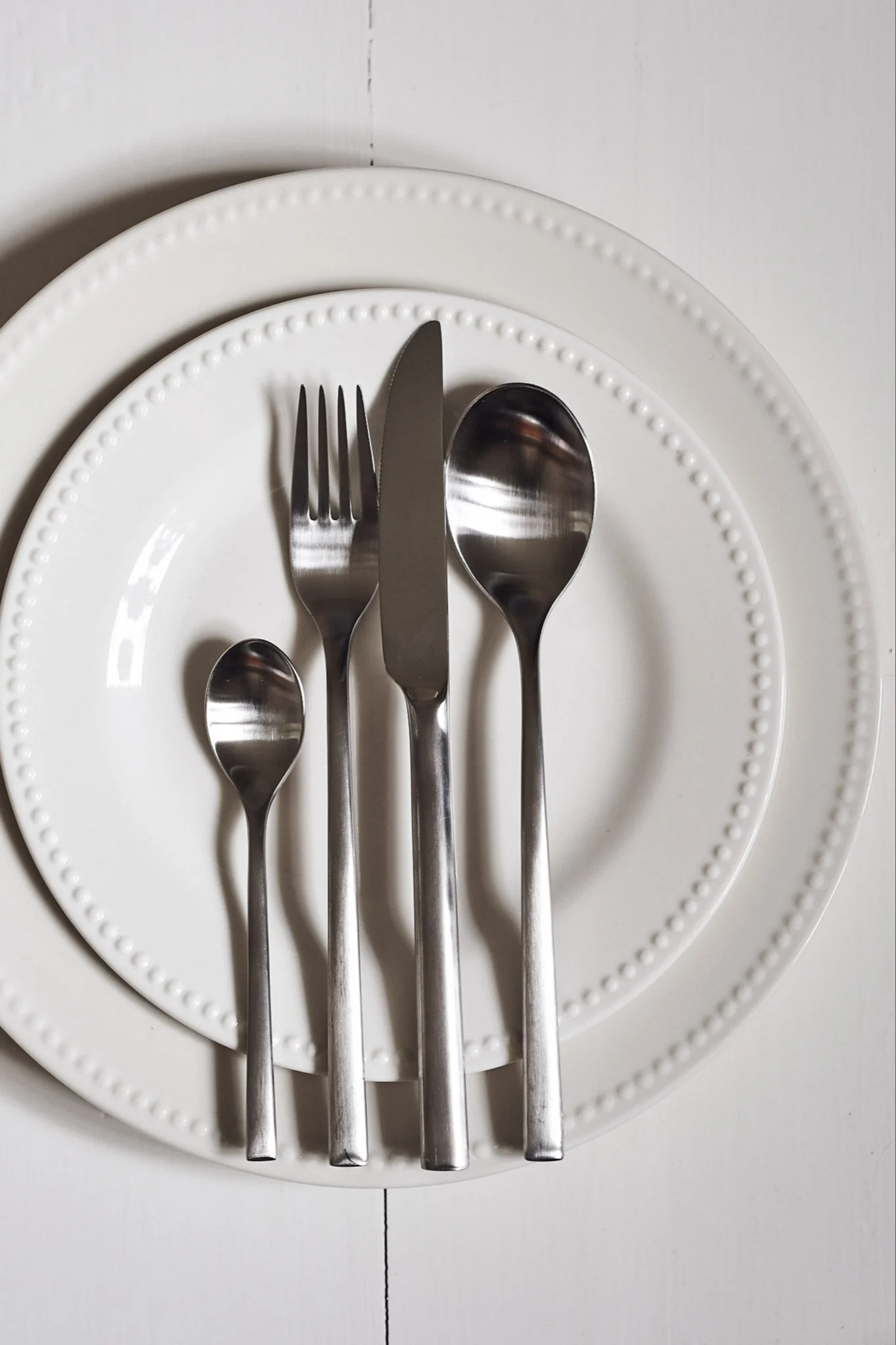 Table setting with two white plates and four pieces of silver cutlery arranged vertically.