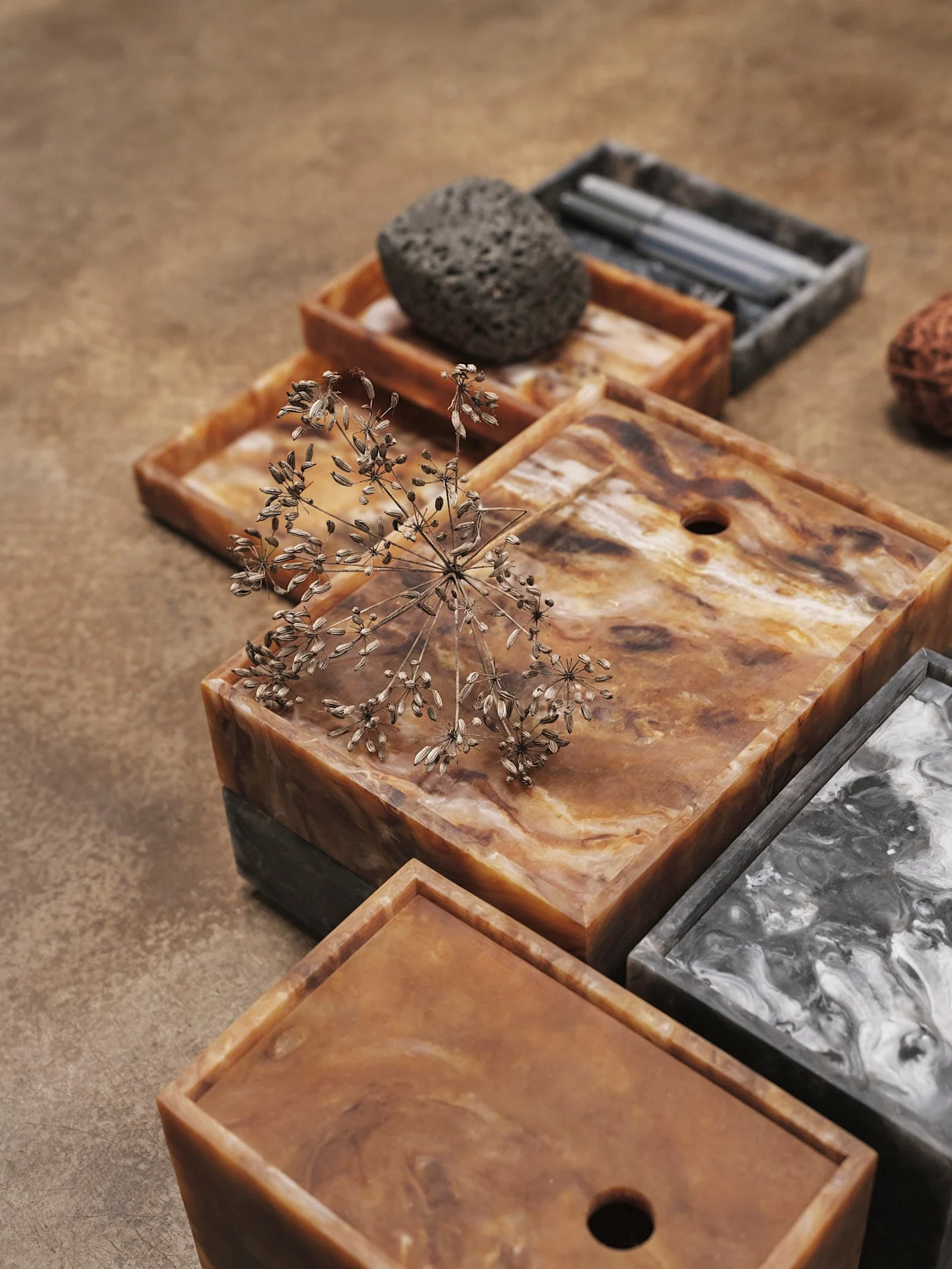 Stacked decorative trays with swirled brown, orange, and grey patterns, adorned with a dried botanical element.
