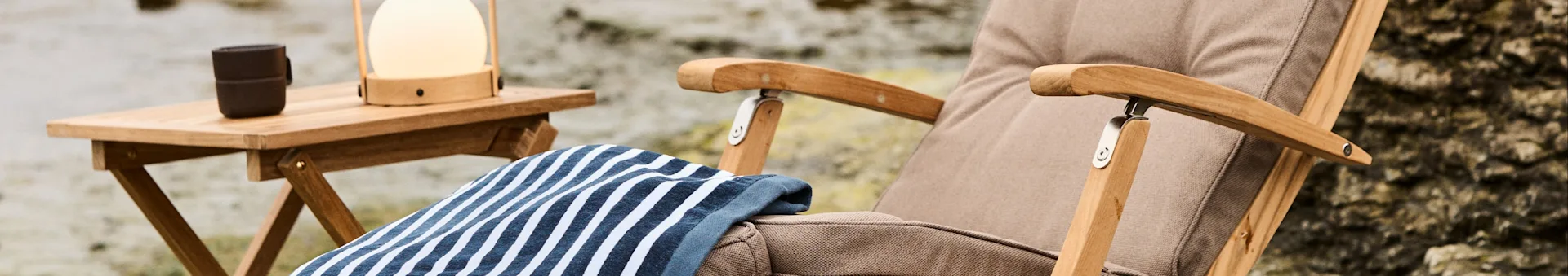 Outdoor lounge chair with a striped towel and a side table with a lamp and mug.