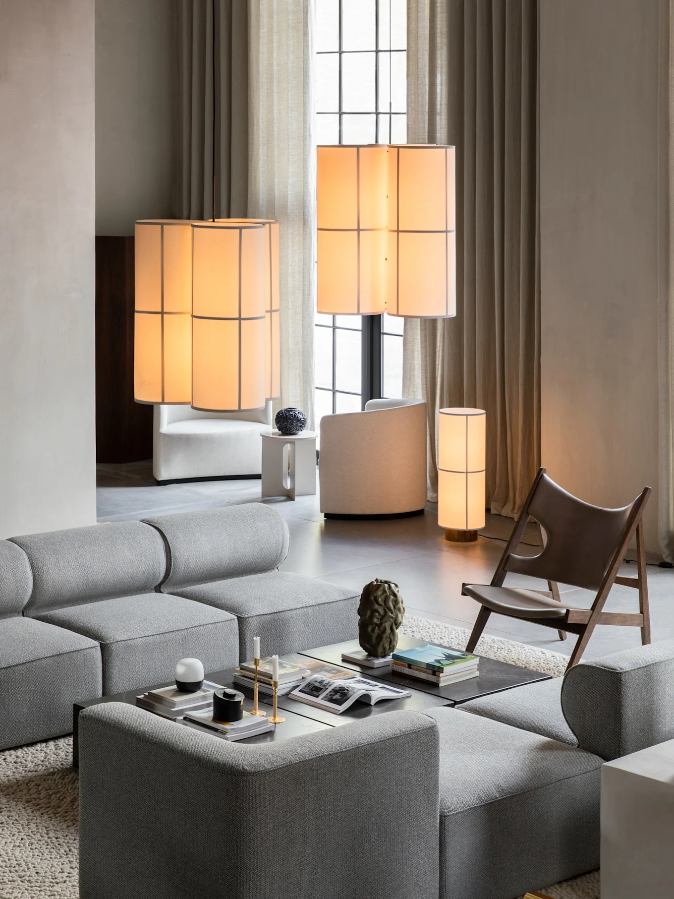 Modern living room with a grey modular sofa, coffee table, brown leather lounge chair, and multiple illuminated lamps.