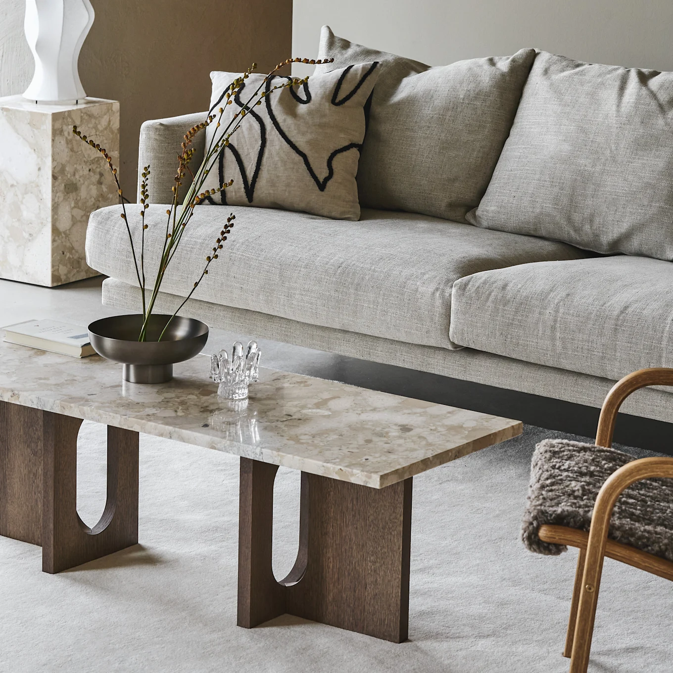 A light grey sofa, marble coffee table with wooden legs, and decorative accessories in a neutral living room.