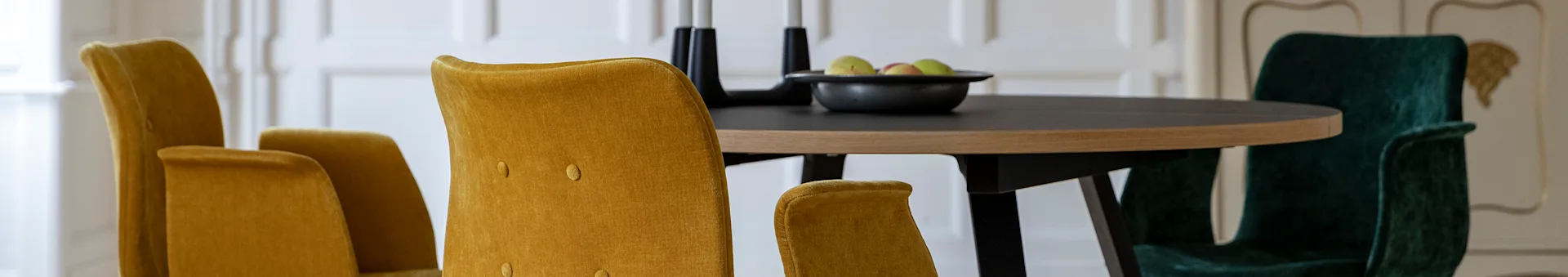 Dining table with mustard yellow and dark green velvet chairs, a fruit bowl, and candle holders.