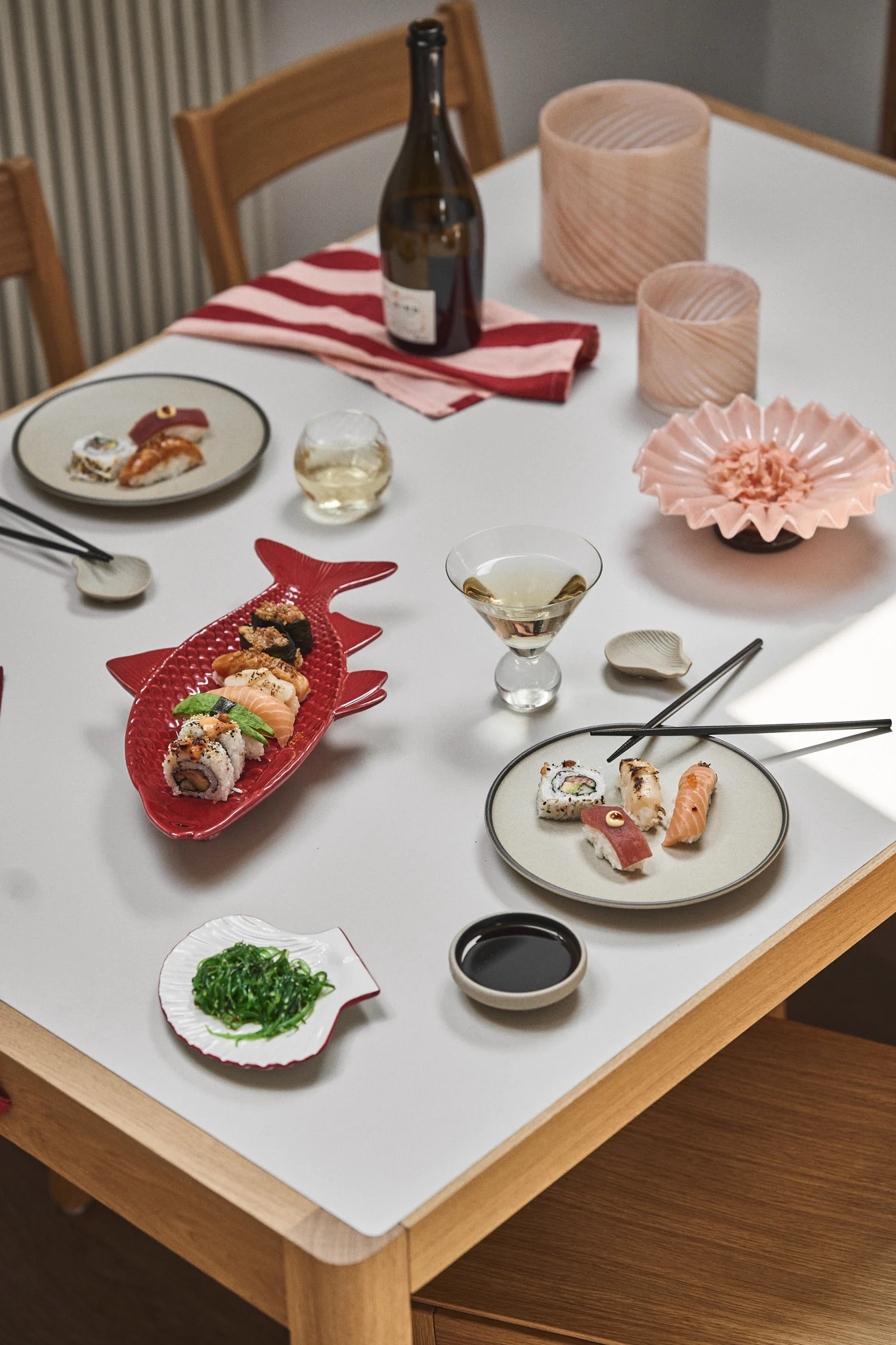 A table set with various sushi platters, including a red fish-shaped dish, a wine bottle, and drinks.