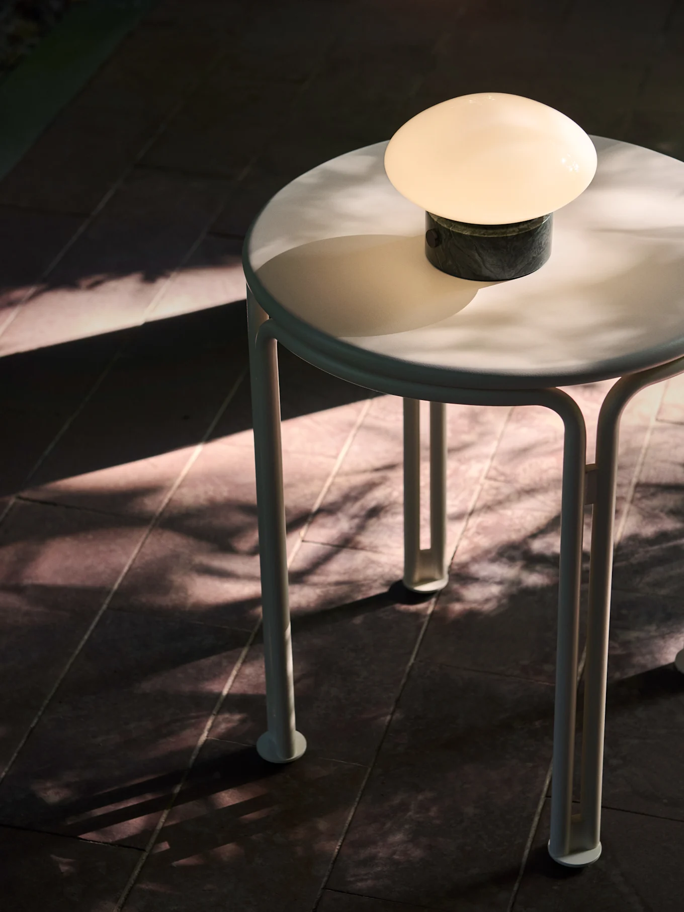 A small round table with a glowing mushroom-shaped lamp, dramatic sun and leaf shadows.
