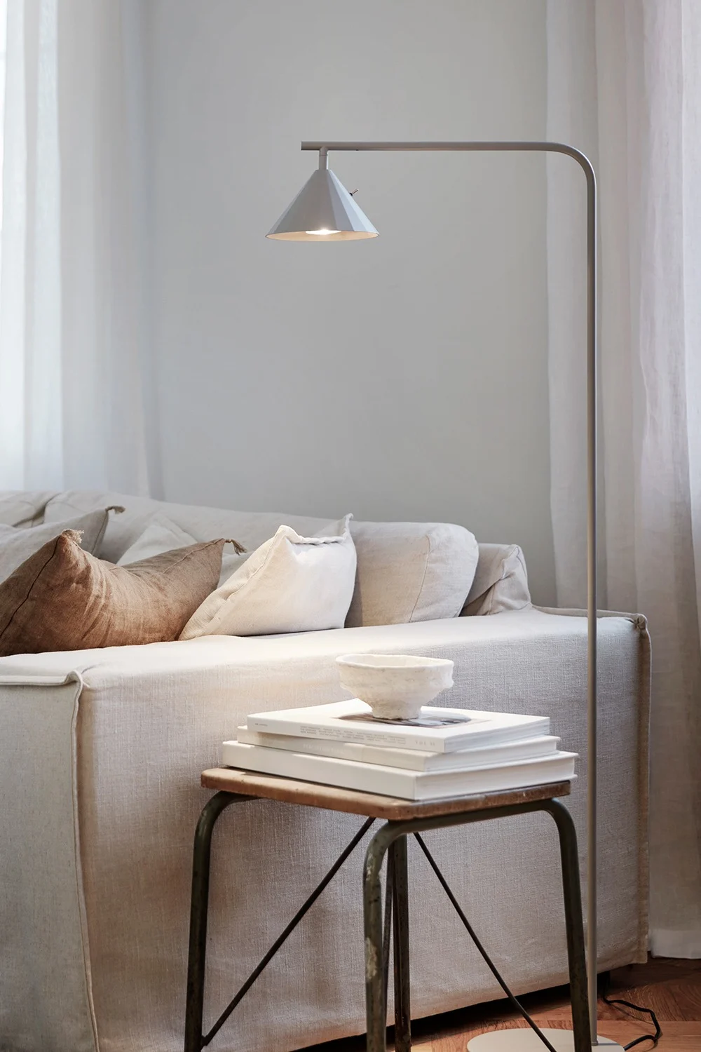A cozy living room with a light-colored linen sofa, a floor lamp, and a side table with books and a bowl.