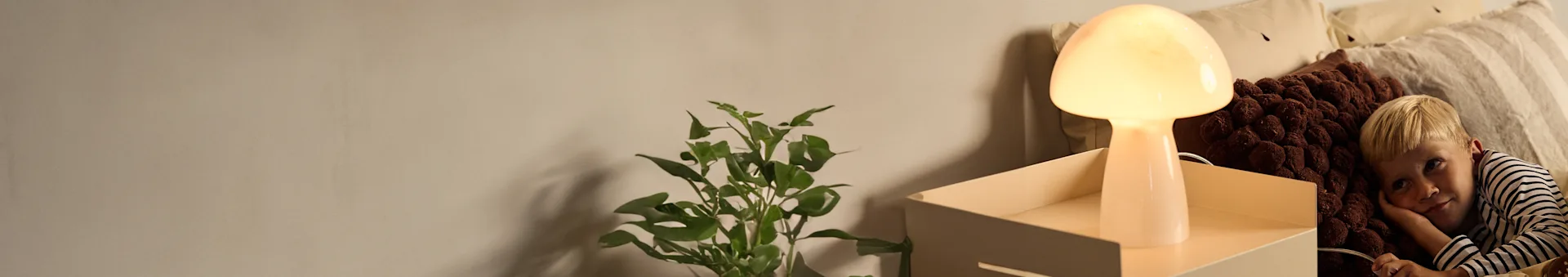 Boy in striped shirt lying in bed with a glowing mushroom lamp and plant.