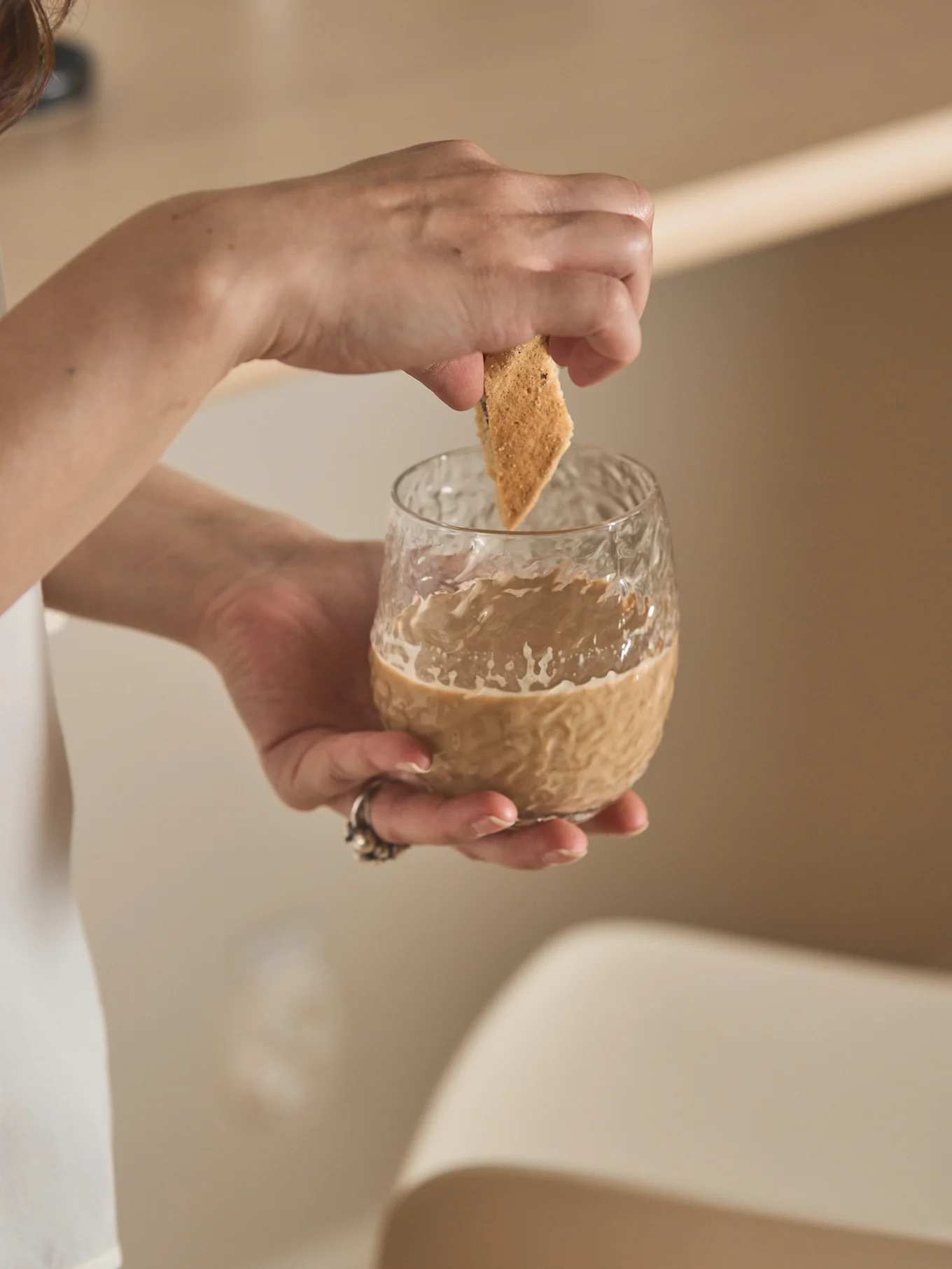 Hands dipping a triangular biscuit into a glass of creamy coffee.