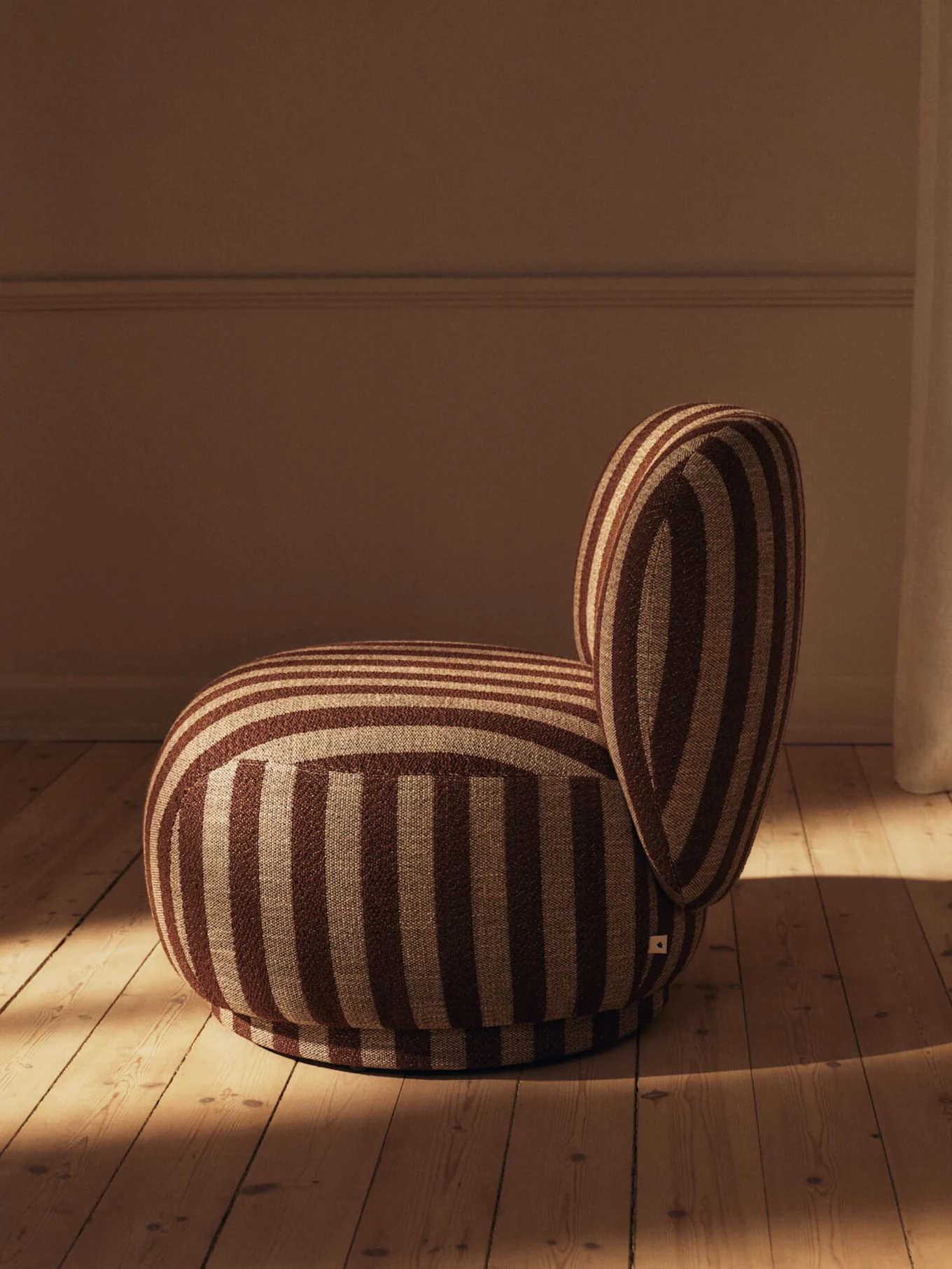 Rounded brown and beige striped armchair with a curved backrest on a light wooden floor.