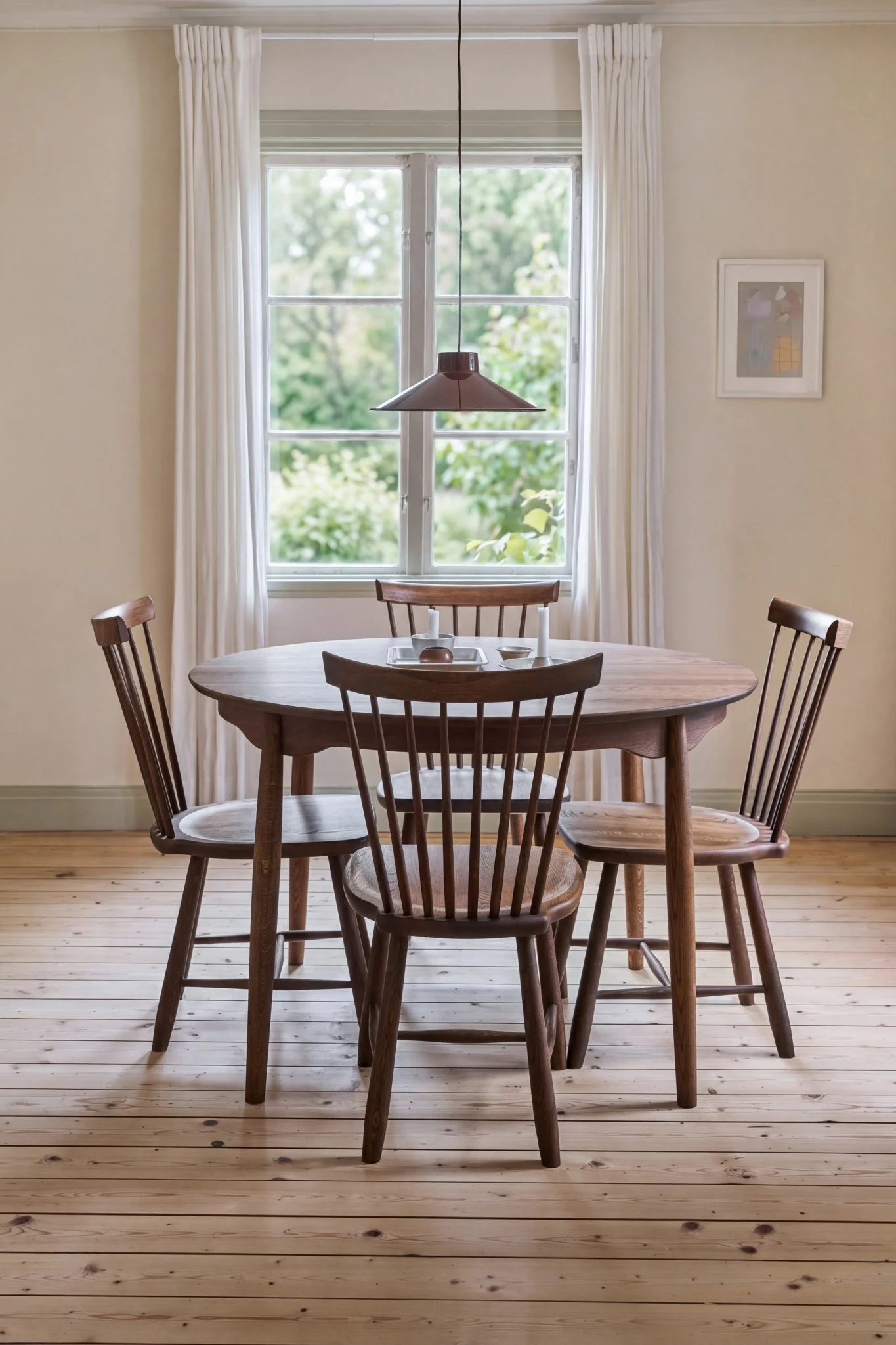 A cozy dining room with a round wooden table, four wooden chairs, a window with white curtains, and a pendant lamp.