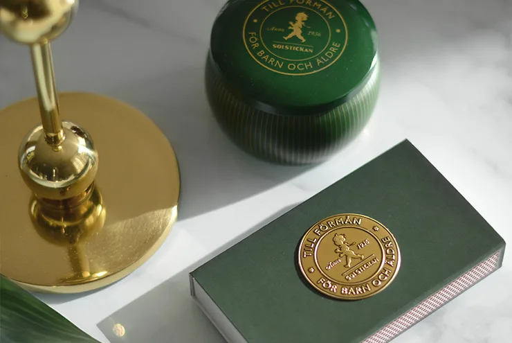Green ribbed tin and matchbox with gold emblems, a golden candlestick base, on a marble surface.