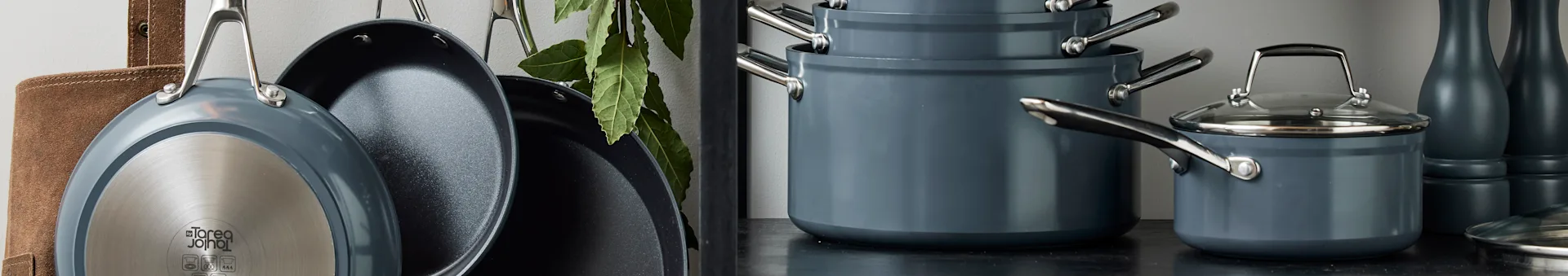 A collection of dark gray non-stick pots and pans, some hanging, others stacked on a dark counter with vases.