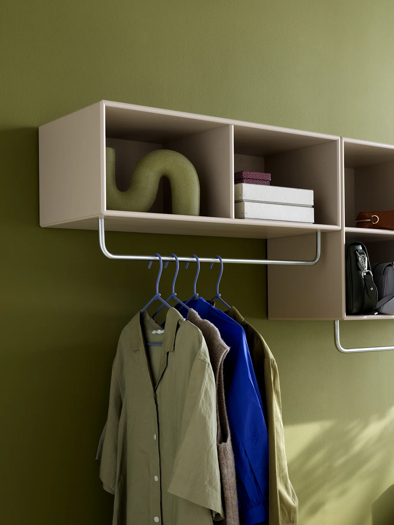 Wall-mounted shelving unit with clothes rail, featuring a green vase, boxes, handbags, and various garments on hangers.