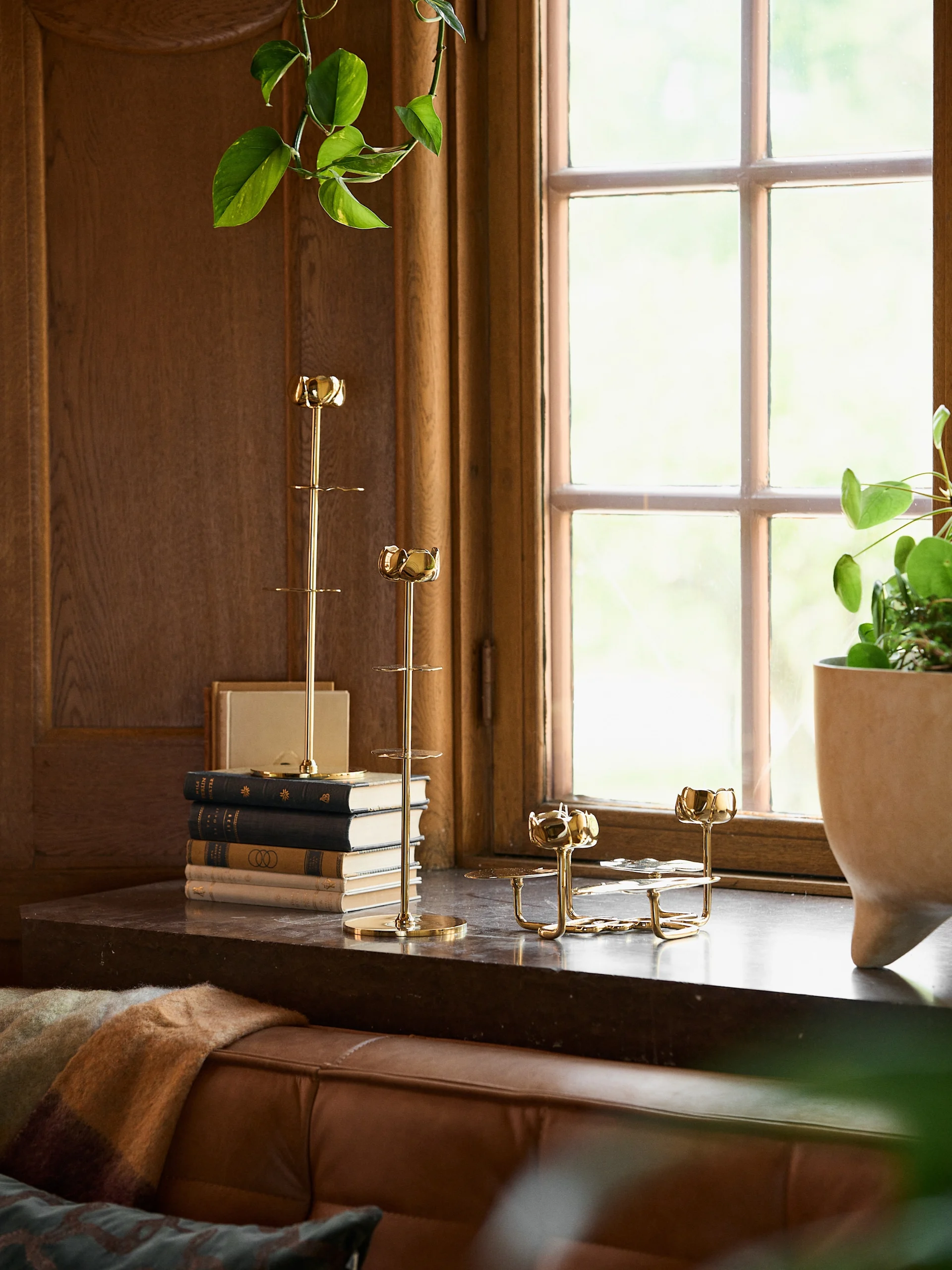 Two golden tiered decorative stands, a stack of books, and a potted plant on a wooden windowsill.
