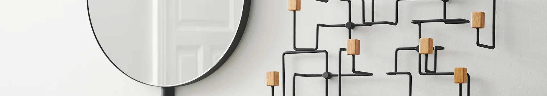 A modern wall-mounted coat rack with black metal frames and light wooden pegs, next to a partial round mirror.