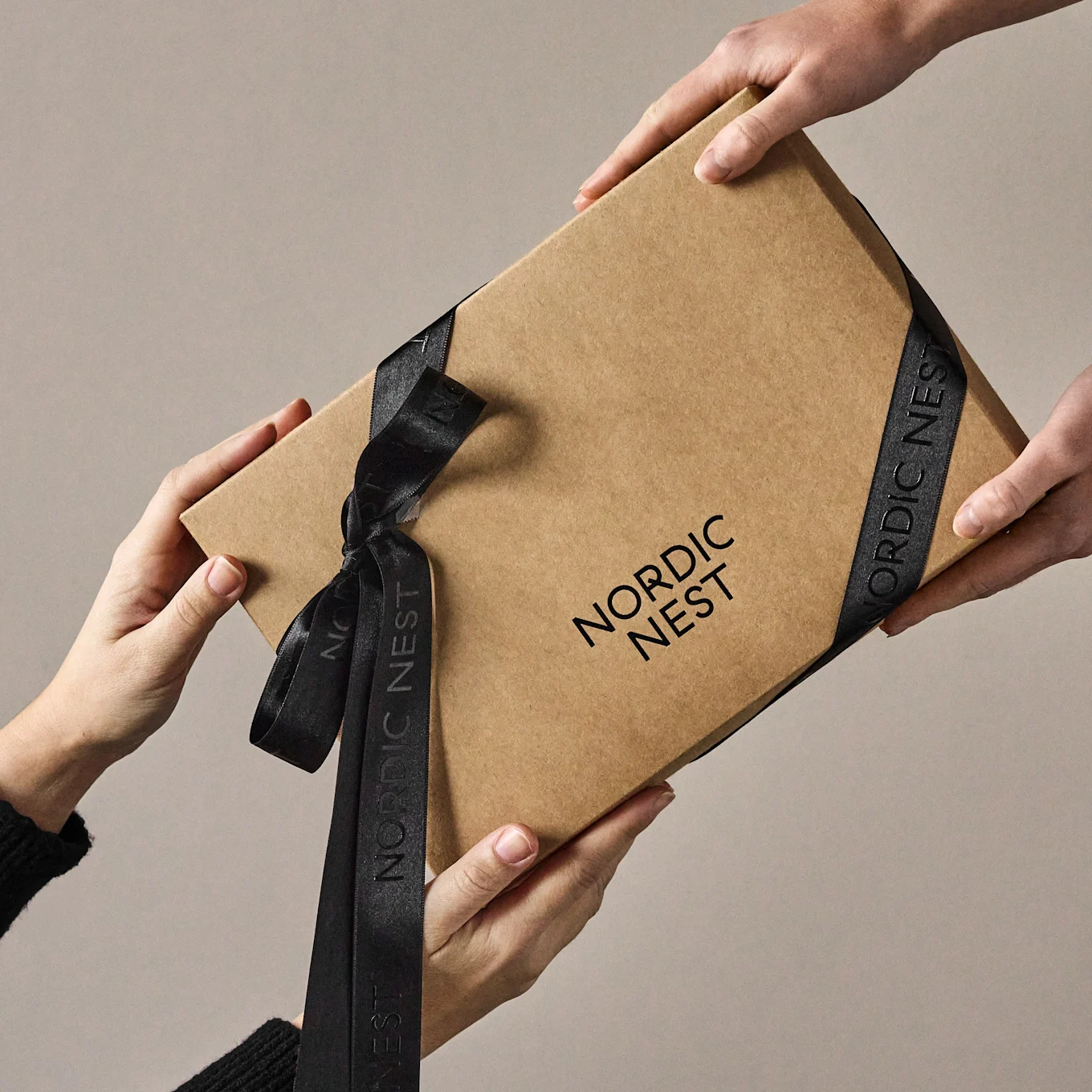 Hands exchanging a brown gift box with 'Nordic Nest' logo and black ribbon.